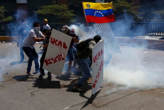 Anti-government protesters take cover behind makeshift shields as they are engulfed in teargas fired by the police in Caracas