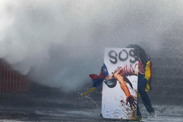 An anti-government protester takes cover behind a makeshift shield from police water cannon in Caracas