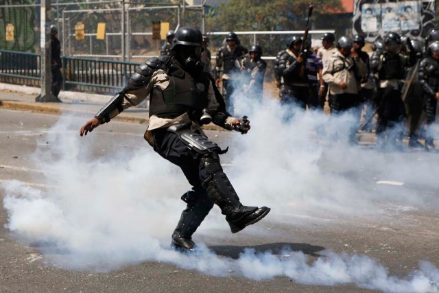 A riot police officer kicks away a tear gas canister during clashes with anti-government protesters in Caracas