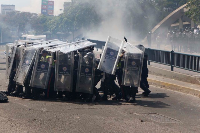 Riot police take cover during clashes with anti-government protesters in Caracas