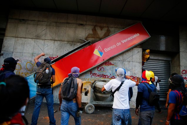Anti-government protesters bring down a banner of Banco de Venezuela during riots in Caracas