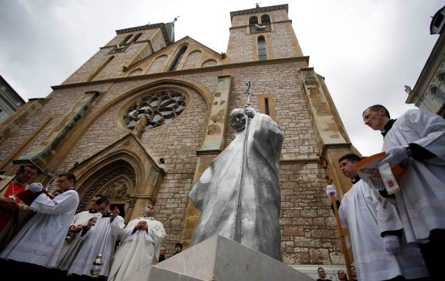 Priests stand in front of a church during an unveiling ceremony of a statue of the late Pope John Paul II in Sarajevo