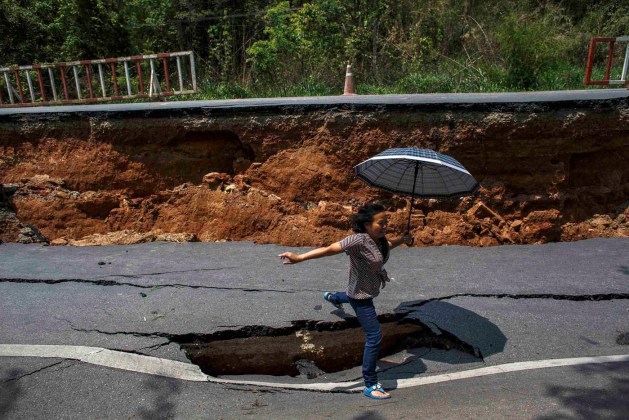 Una mujer con un paraguas salta sobre un agujero en un camino de la carretera, dañado por el terremoto del lunes en Chiang Rai, en el norte de Tailandia / Reuters