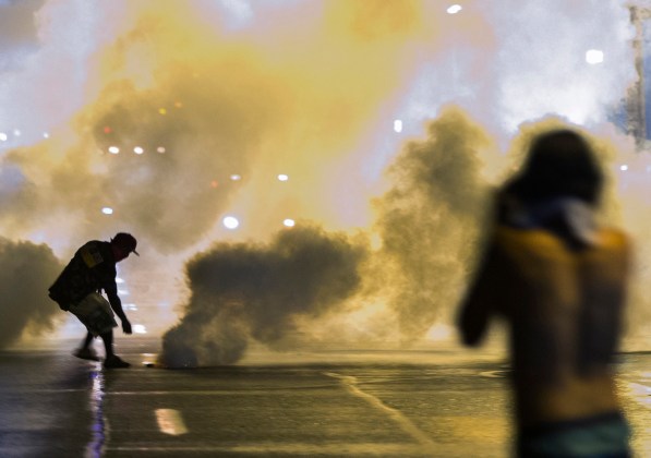A protester reaches down to throw back a smoke canister as police clear a street after the passing of a midnight curfew in Ferguson