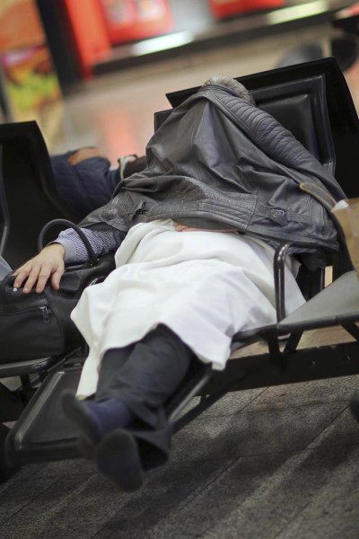 Un pasajero se cubre la cara con una chaqueta mientras aprovecha para descansar hasta conocer noticias de su vuelo con compañía alemana Lufthansa en el aeropuerto de Fráncort (Alemania). (Foto EFE/Fredrik Von Erichsen)