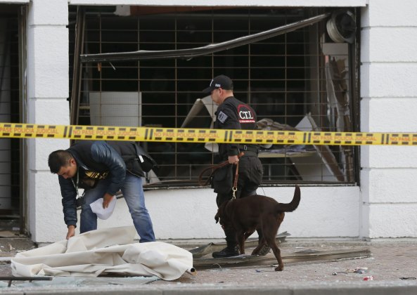 Policemen inspect the site of an explosion with a bomb sniffing dog, in front of the office of the Porvenir pension fund in downtown Bogota