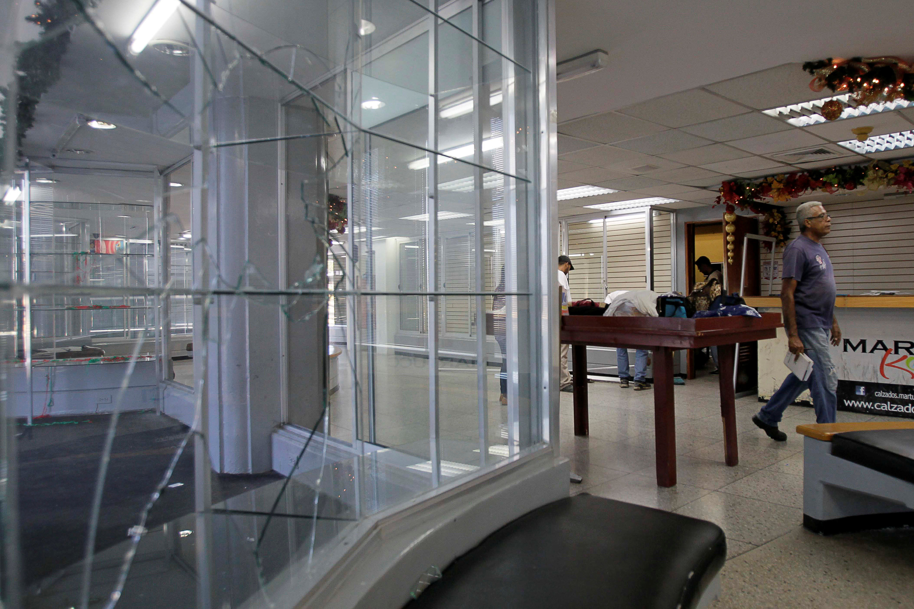 People walk next to broken showcases after a shoe shop was looted in Maracaibo