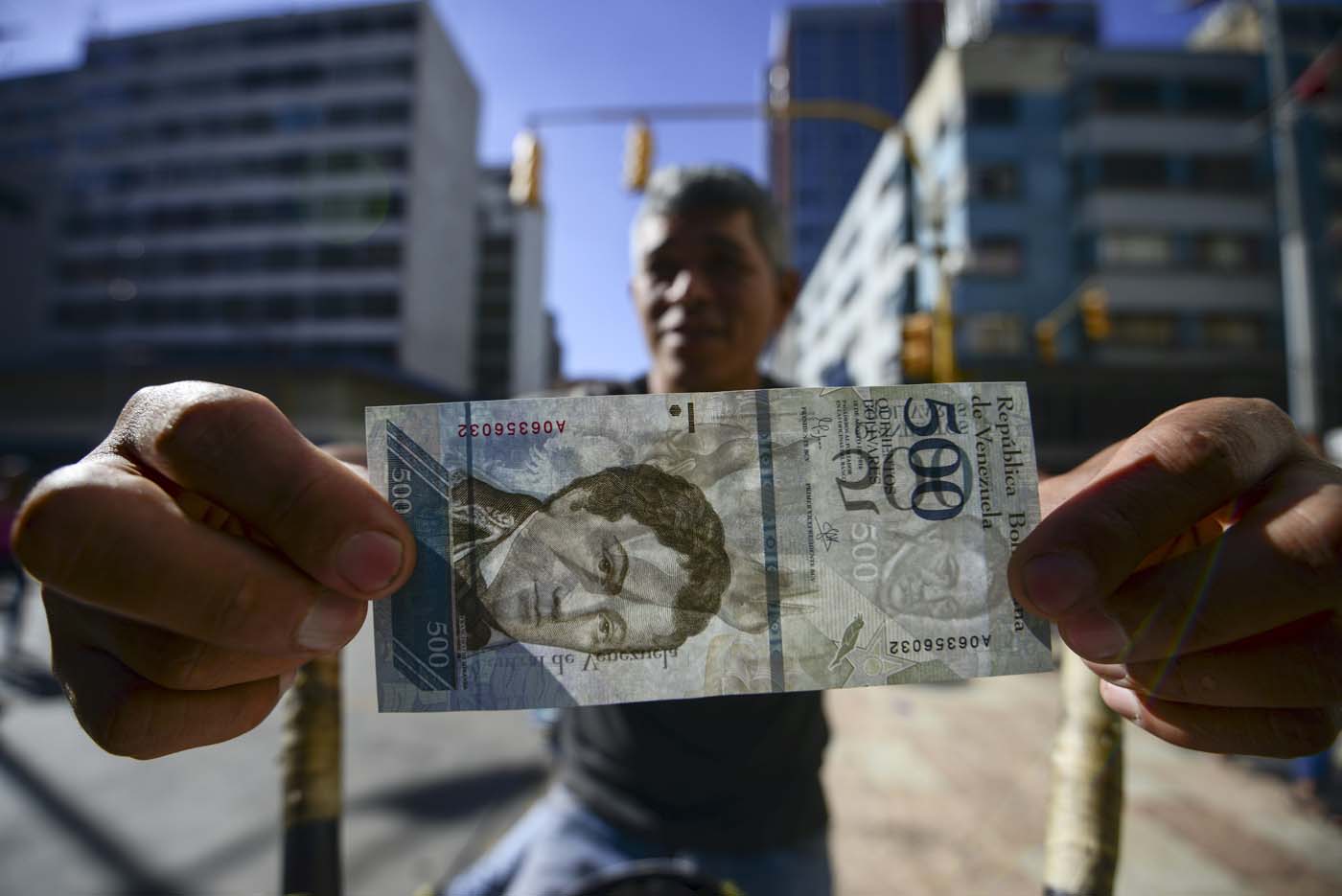 A street coffee vendor shows a new 500-Bolivar-note (74 cents of US dollar) in Caracas on January 16, 2017. A new family of currency will progressively come into circulation in the South American country that has the highest inflation rate in the world, which IMF forecasts say could soon hit 475 percent. / AFP PHOTO / JUAN BARRETO