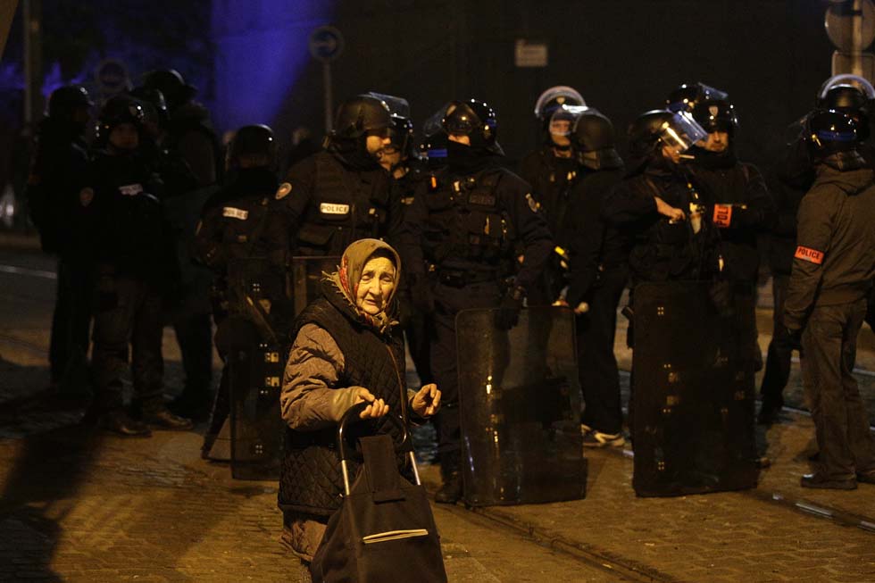 A elderly woman passes as anti riot police officers stand guard during a protest in Bobigny, a district of northeast Paris, to denounce police brutality after a black man was allegedly sodomised with a baton during an arrest while in their custody in Paris on February 11, 2017. A 22-year-old black youth worker named as Theo, a talented footballer with no criminal record, required surgery after his arrest on February 2, 2017 when he claims a police officer sodomized him with his baton. One officer has been charged with rape and three others with assault over the incident in the tough northeastern suburb of Aulnay-sous-Bois which has revived past controversies over alleged police brutality. / AFP PHOTO / GEOFFROY VAN DER HASSELT