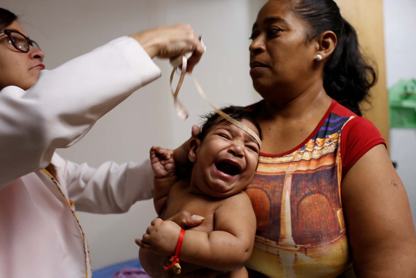 Iberis Vargas (R), holds her 7-month-old daughter, Geovelis Ramos, a neurological patient being treated with anticonvulsants, while an specialist examines her in a clinic in La Guaira, Venezuela February 4, 2017. REUTERS/Carlos Garcia Rawlins    SEARCH "EPILEPSY CARACAS" FOR THIS STORY. SEARCH "WIDER IMAGE" FOR ALL STORIES.