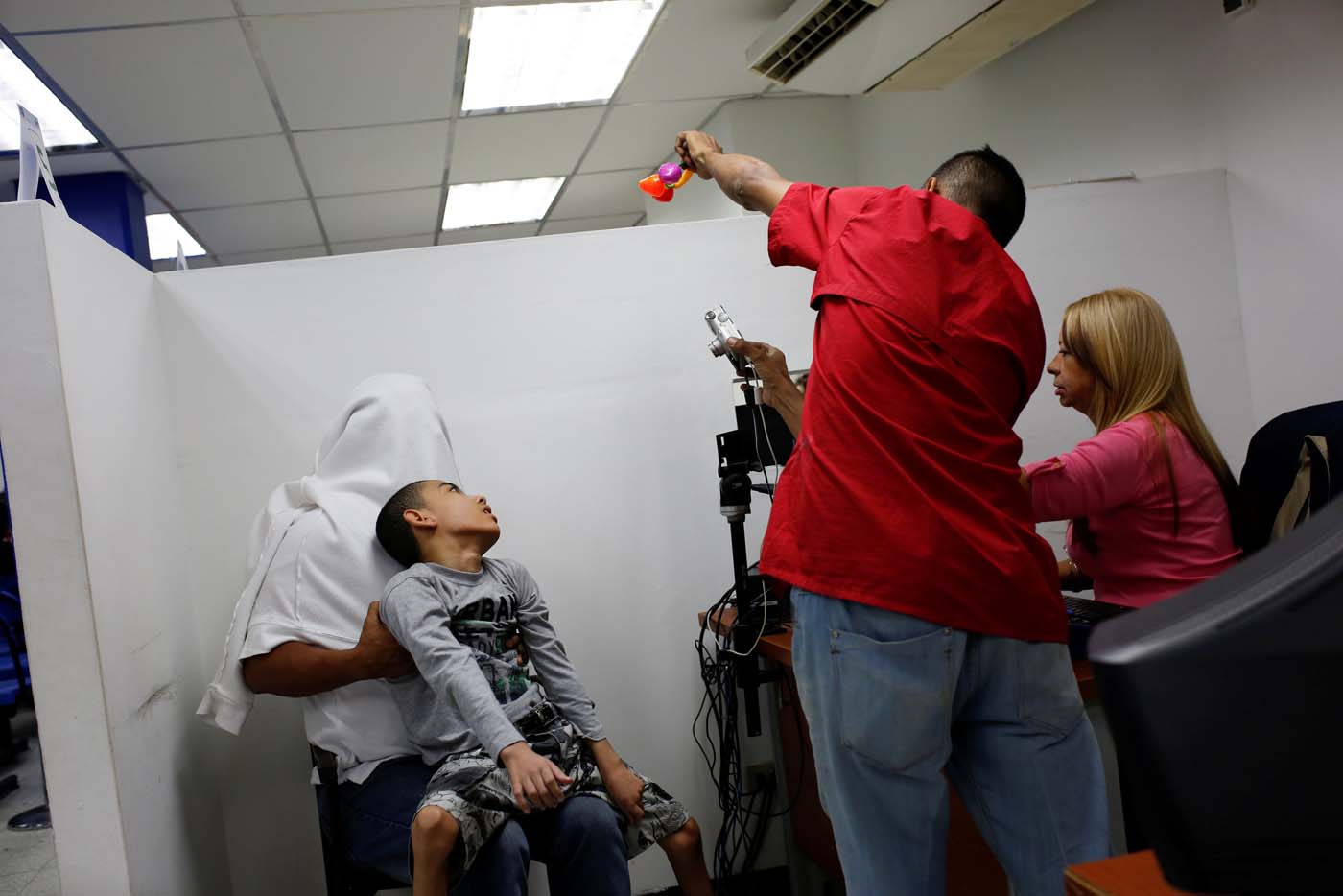 Miguel Anton (L covered) holds his son, Jose Gregorio Anton, 11, a neurological patient being treated with anticonvulsants, while workers takes a picture to him for his ID in La Guaira, Venezuela February 20, 2017. REUTERS/Carlos Garcia Rawlins    SEARCH "EPILEPSY CARACAS" FOR THIS STORY. SEARCH "WIDER IMAGE" FOR ALL STORIES.