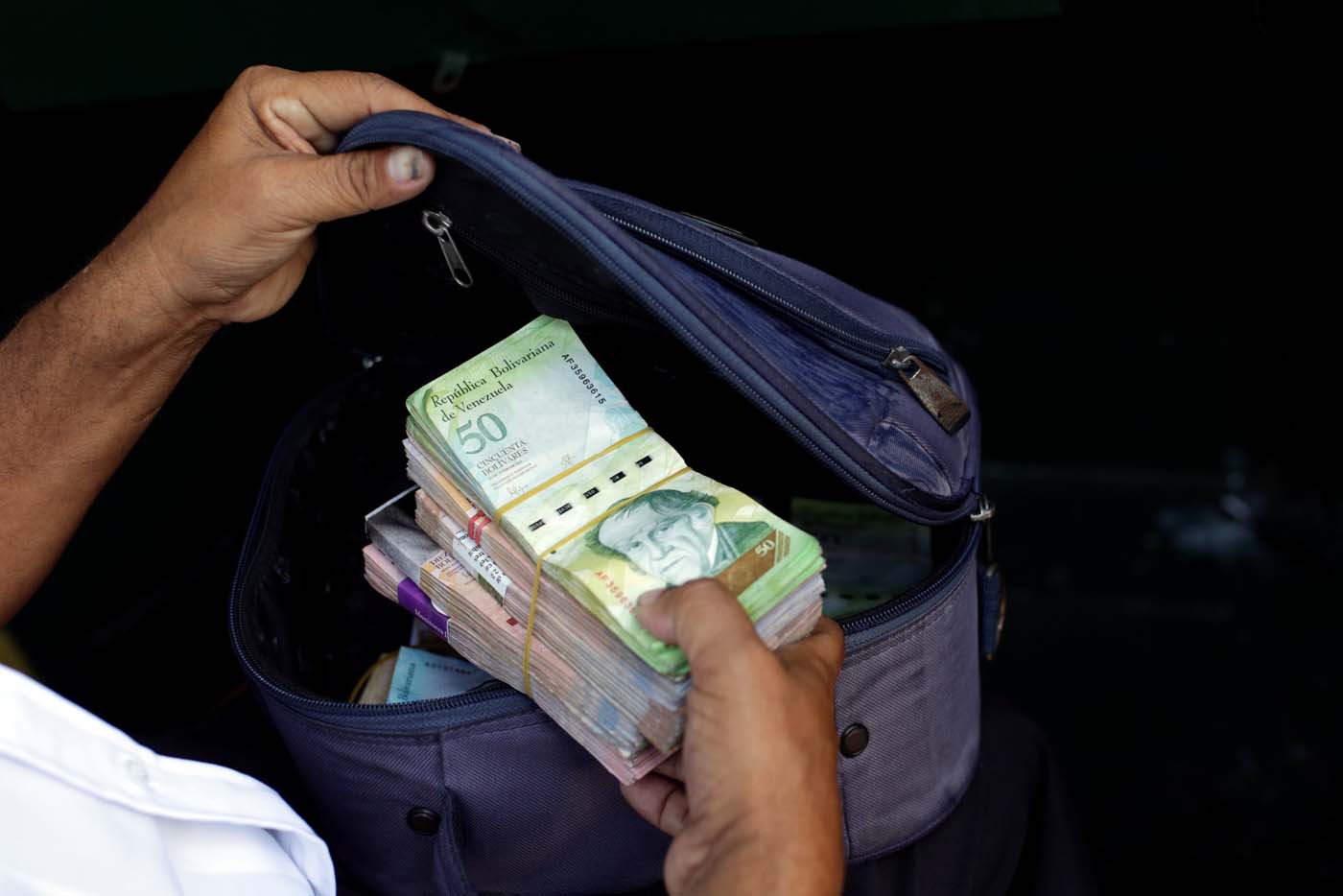 A man places banknotes in a pouch after withdrawing them from a bank branch in Caracas, Venezuela March 21, 2017. REUTERS/Marco Bello