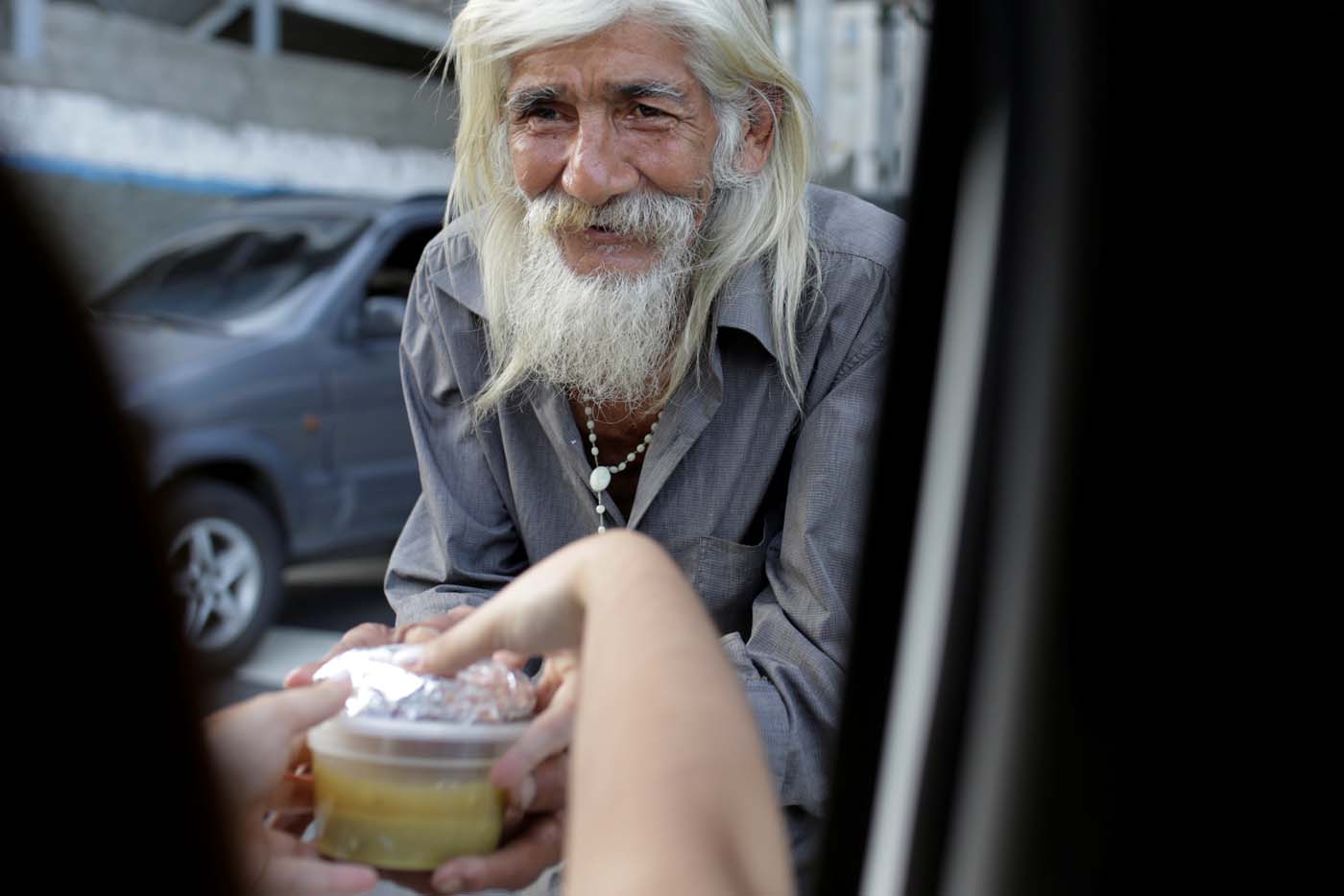 A volunteer of Make The Difference (Haz La Diferencia) charity initiative gives through a car's window a cup of soup to a homeless man in a street of Caracas, Venezuela March12, 2017. Picture taken March 12, 2017. REUTERS/Marco Bello