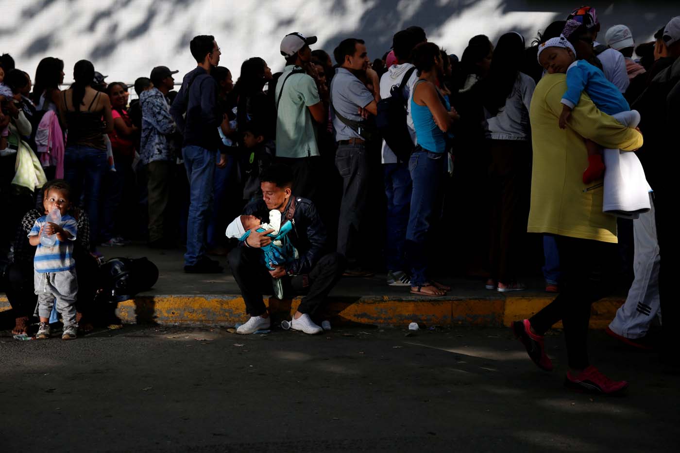 A man carrying a baby rests on the sidewalk as he queues to try and buy diapers outside a pharmacy in Caracas, Venezuela March 18, 2017. REUTERS/Carlos Garcia Rawlins SEARCH "GARCIA QUEUEING" FOR THIS STORY. SEARCH "WIDER IMAGE" FOR ALL STORIES. TPX IMAGES OF THE DAY.