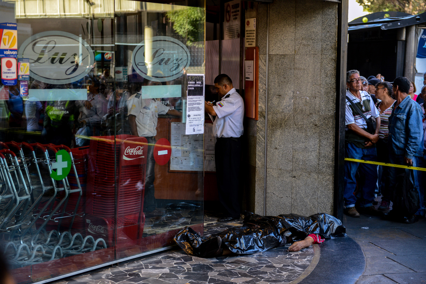 The body of a man lies outside a supermarket, where he died of a heart attack after waiting in a long line to buy food, in Caracas on March 30, 2017. / AFP PHOTO / FEDERICO PARRA
