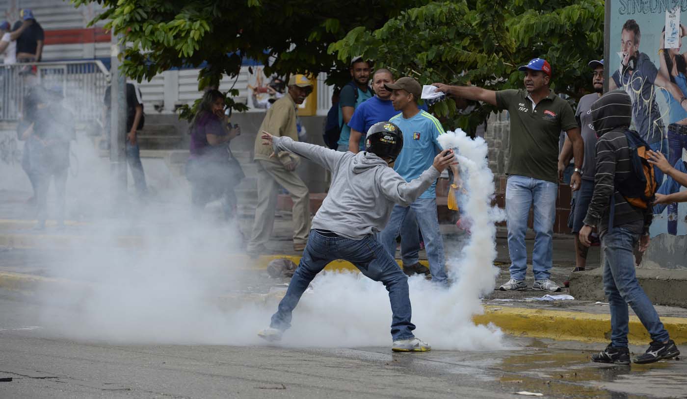 An opposition activist throws back tear gas during a march against President Nicolas Maduro, in Caracas on May 1, 2017. Security forces in riot vans blocked off central Caracas Monday as Venezuela braced for pro- and anti-government May Day protests one month after a wave of deadly political unrest erupted. / AFP PHOTO / FEDERICO PARRA