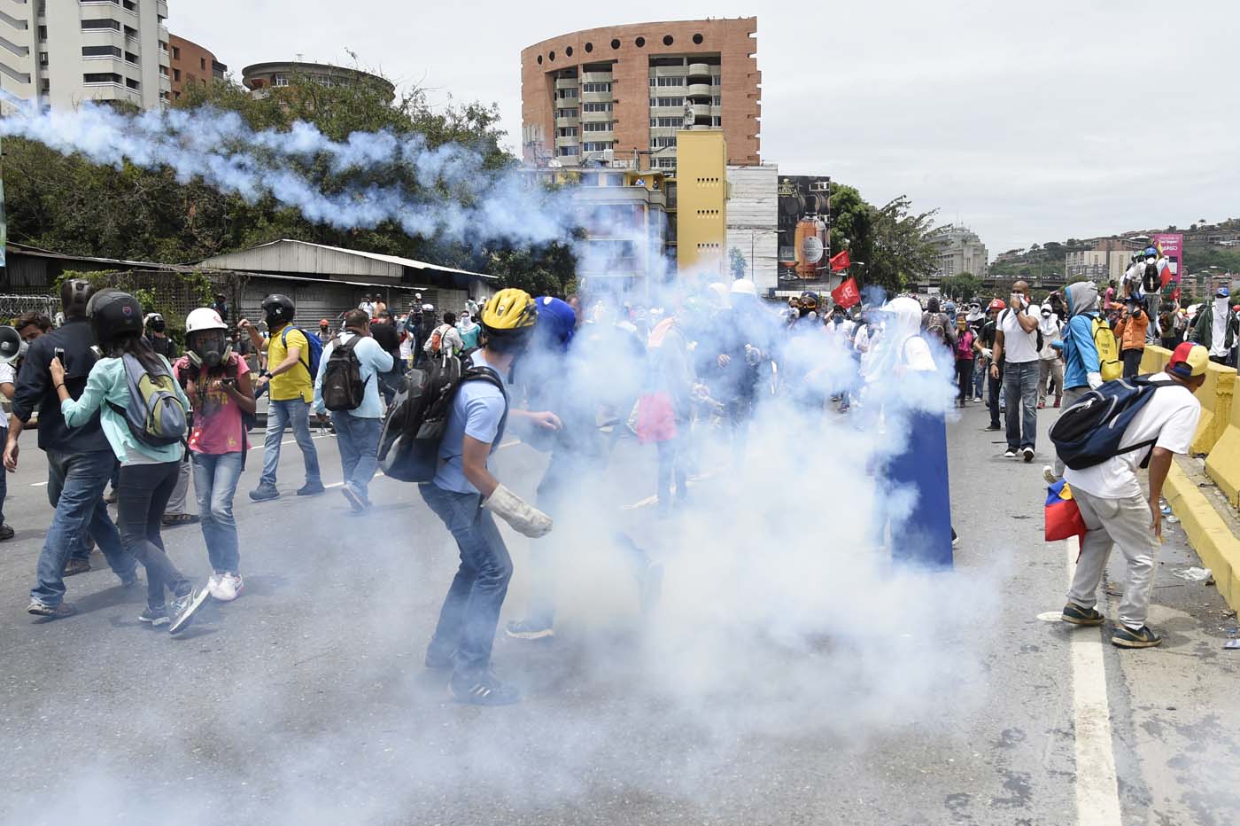 Demonstrators march amid tear gas during a protest against Venezuelan President Nicolas Maduro, in Caracas on May 3, 2017. Venezuela's angry opposition rallied Wednesday vowing huge street protests against President Nicolas Maduro's plan to rewrite the constitution and accusing him of dodging elections to cling to power despite deadly unrest. / AFP PHOTO / JUAN BARRETO