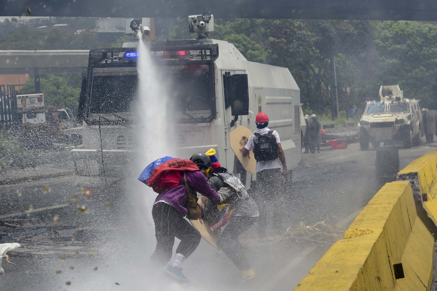 Demonstrators are sprayed by a riot police water cannon during clashes within a protest against Venezuelan President Nicolas Maduro, on May 3, 2017. Venezuela's angry opposition rallied Wednesday vowing huge street protests against President Nicolas Maduro's plan to rewrite the constitution and accusing him of dodging elections to cling to power despite deadly unrest. / AFP PHOTO / RONALDO SCHEMIDT