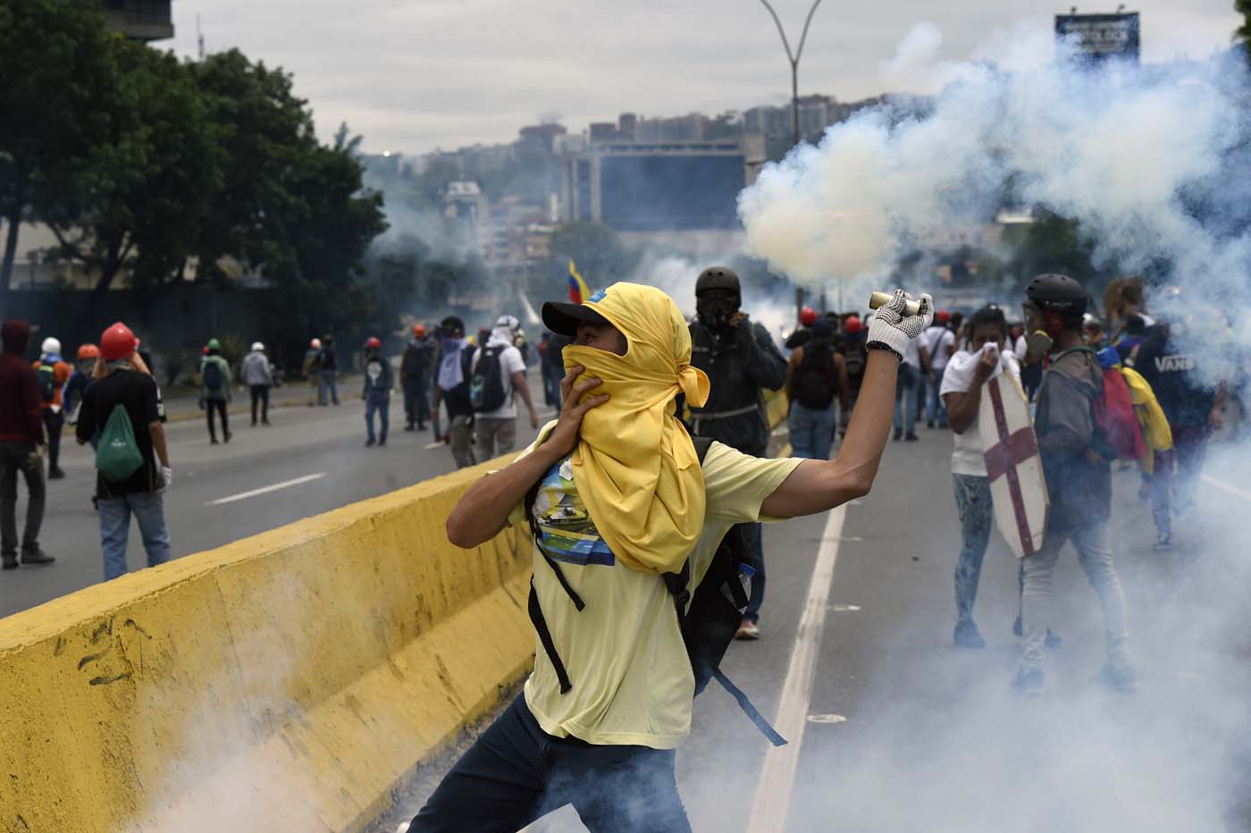 A demonstrator throws back tear gas to the police, during clashes within a protest against Venezuelan President Nicolas Maduro, in Caracas on May 3, 2017. Venezuela's angry opposition rallied Wednesday vowing huge street protests against President Nicolas Maduro's plan to rewrite the constitution and accusing him of dodging elections to cling to power despite deadly unrest. / AFP PHOTO / JUAN BARRETO