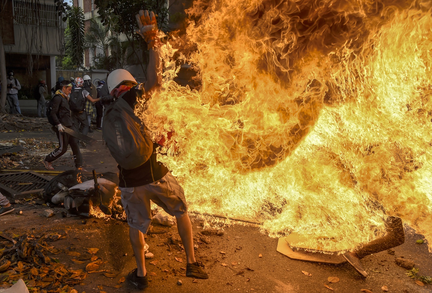 A man tries to help a fellow demonstrator who catched fire, after the gas tank of a police motorbike exploded, during clashes in a protest against Venezuelan President Nicolas Maduro, in Caracas on May 3, 2017. Venezuela's angry opposition rallied Wednesday vowing huge street protests against President Nicolas Maduro's plan to rewrite the constitution and accusing him of dodging elections to cling to power despite deadly unrest. / AFP PHOTO / JUAN BARRETO