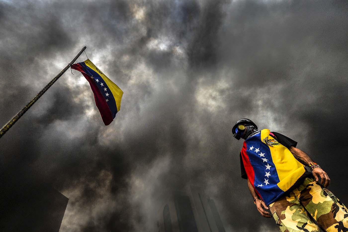 An anti-government demonstrator stands next to a national flag during an opposition protest blocking the Francisco Fajardo highway in Caracas on May 27, 2017. Demonstrations that got underway in late March have claimed the lives of 58 people, as opposition leaders seek to ramp up pressure on Venezuela's leftist president, whose already-low popularity has cratered amid ongoing shortages of food and medicines, among other economic woes. / AFP PHOTO / LUIS ROBAYO