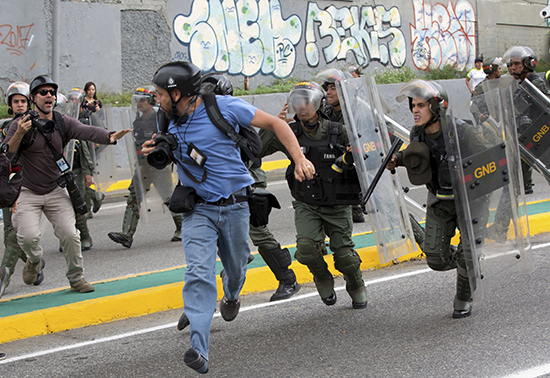 Reuters photojournalist Marco Bello runs as Venezuelan National Guard soldiers chase him during a protest outside the Supreme Court in Caracas, Venezuela, Friday, March 31, 2017. Security forces violently repressed small protests that broke out in Venezuela's capital Friday after the government-stacked Supreme Court gutted congress of its last vestiges of power, drawing widespread condemnation from foreign governments. (AP Photo/Ariana Cubillos)