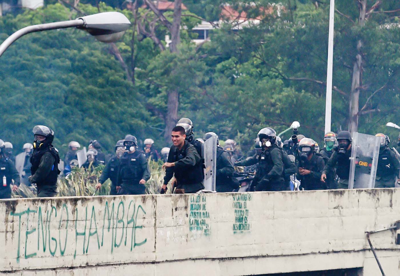 A member of the National Guard holds a gun (C) during clashes with opposition activists demonstrating against the government of President Nicolas Maduro along the Francisco Fajardo highway in Caracas on June 19, 2017. Near-daily protests against President Nicolas Maduro began on April 1, with demonstrators demanding his removal and the holding of new elections. The demonstrations have often turned violent with 73 people killed and more than 1,000 injured so far, prosecutors say, and more than 3,000 arrested, according to the NGO Forum Penal.  / AFP PHOTO / Juan BARRETO