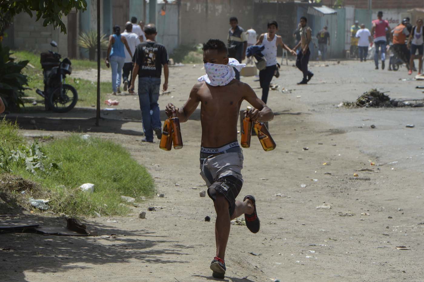 A young man runs carryng stolen alcohol bottles after looting a supermarket in Maracay, Aragua state, Venezuela on June 27, 2017. / AFP PHOTO / Federico Parra