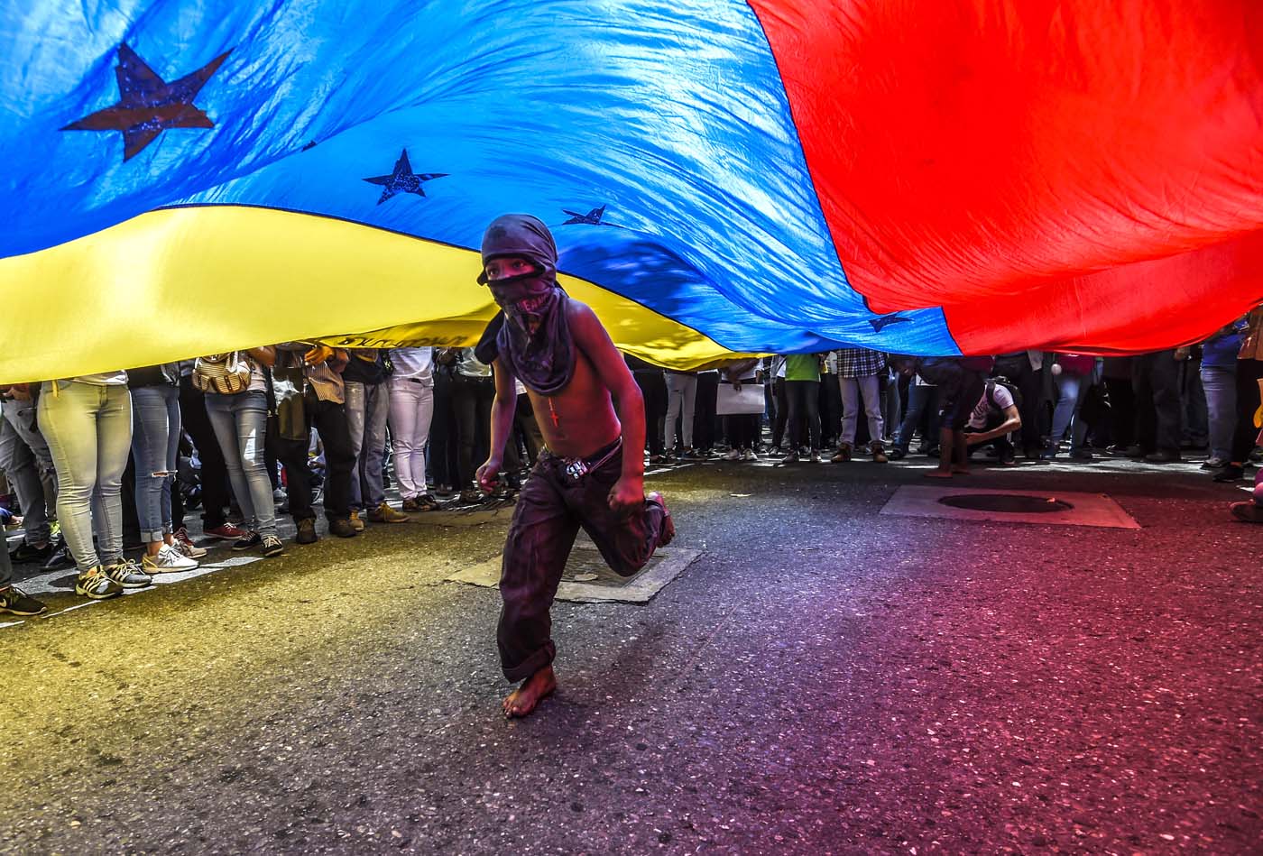 A boy runs under a Venezuelan flag during a protest of journalists and media workers against the attacks on journalists, in Caracas on June 27, 2017. / AFP PHOTO / JUAN BARRETO