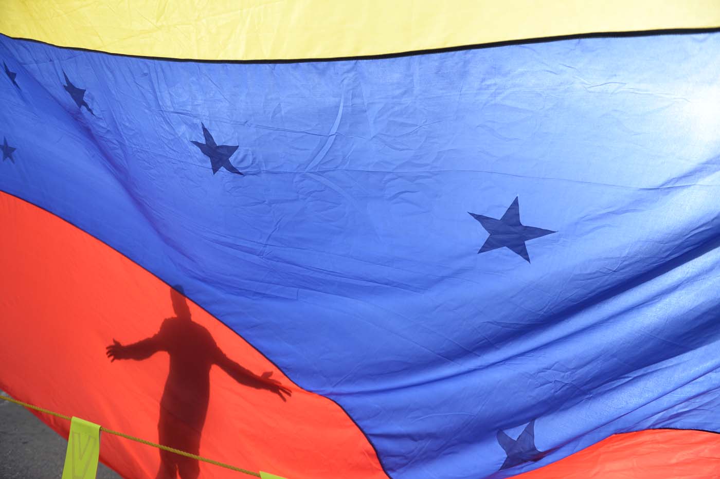 A person's shadow is cast on a Venezuelan national flag in Caracas on July 10, 2017. Venezuela hit its 100th day of anti-government protests Sunday, amid uncertainty over whether the release from prison a day earlier of prominent political prisoner Leopoldo Lopez might open the way to negotiations to defuse the profound crisis gripping the country. / AFP PHOTO / FEDERICO PARRA