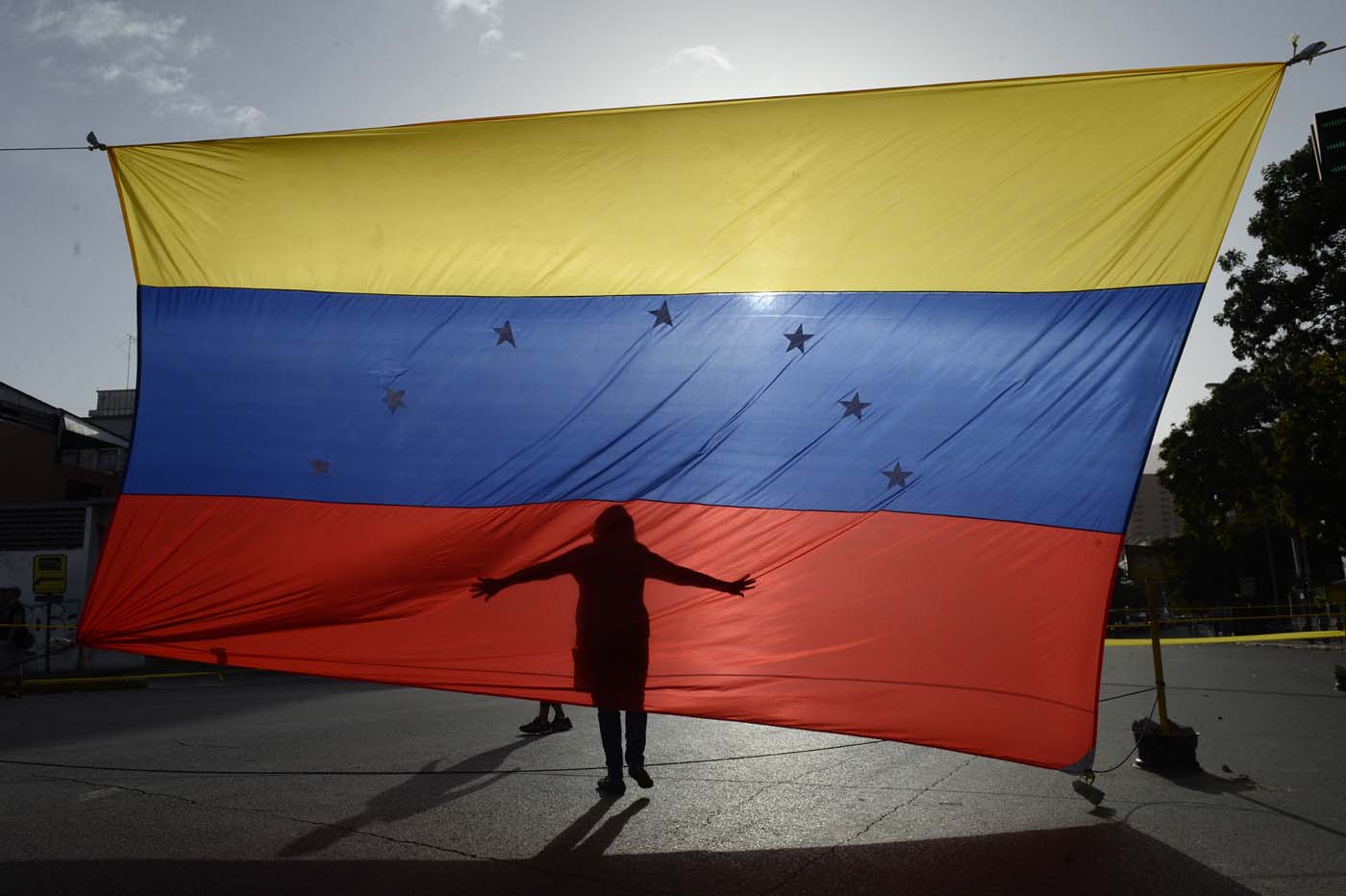 A person's shadow is cast on a Venezuelan national flag in Caracas on July 10, 2017. Venezuela hit its 100th day of anti-government protests Sunday, amid uncertainty over whether the release from prison a day earlier of prominent political prisoner Leopoldo Lopez might open the way to negotiations to defuse the profound crisis gripping the country. / AFP PHOTO / FEDERICO PARRA