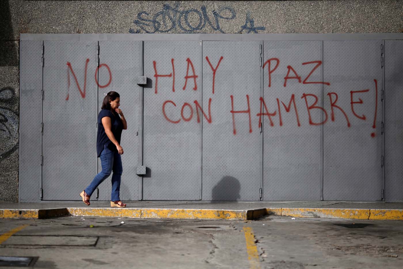 A woman walks in front of a graffiti that reads "There is no peace with hunger" during a strike called to protest against Venezuelan President Nicolas Maduro's government in Caracas, Venezuela, July 20, 2017. REUTERS/Marco Bello