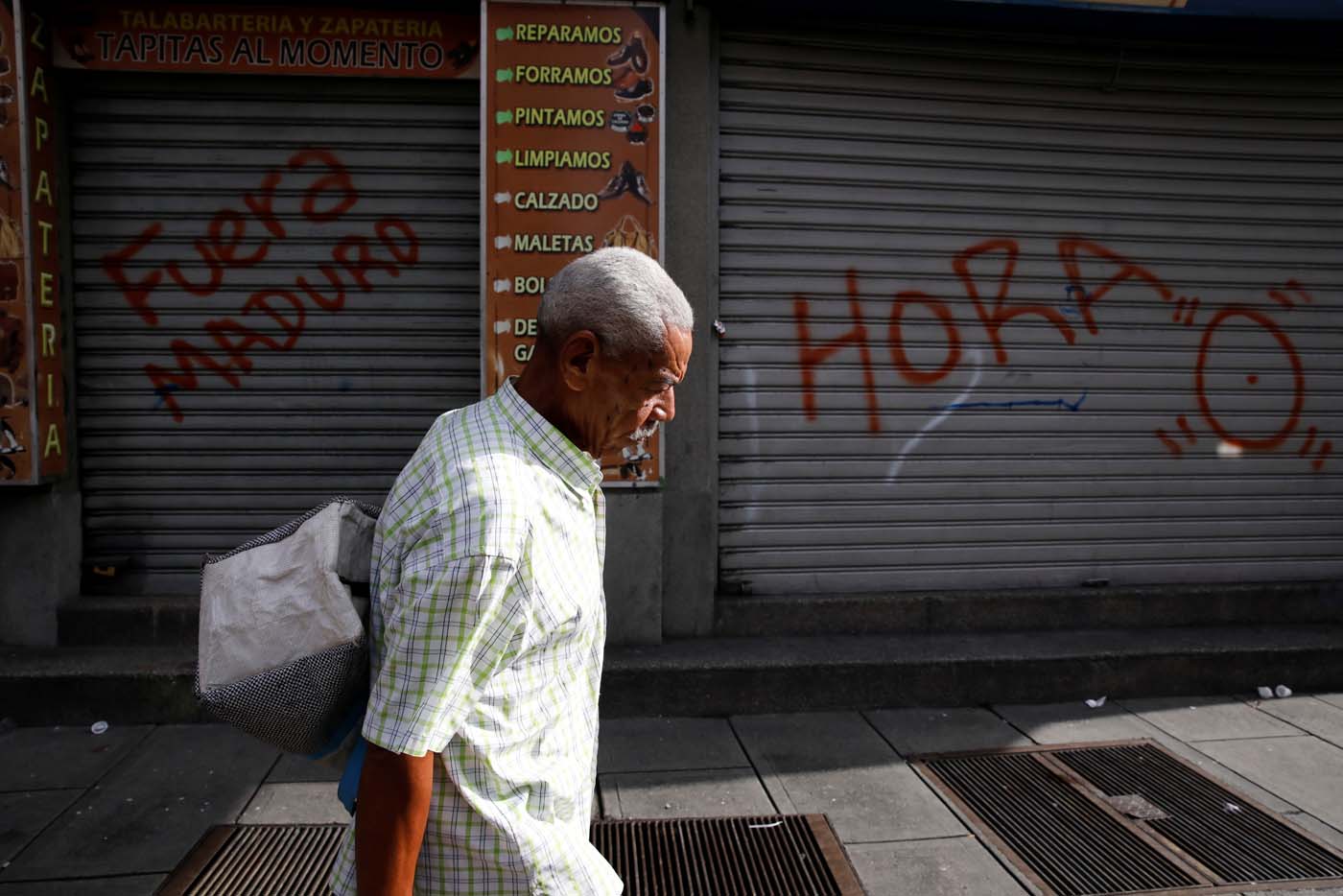 A man walks on the street in front of a graffiti that reads "Maduro leave" during a strike called to protest against Venezuelan President Nicolas Maduro's government in Caracas, Venezuela, July 20, 2017. REUTERS/Carlos Garcia Rawlins