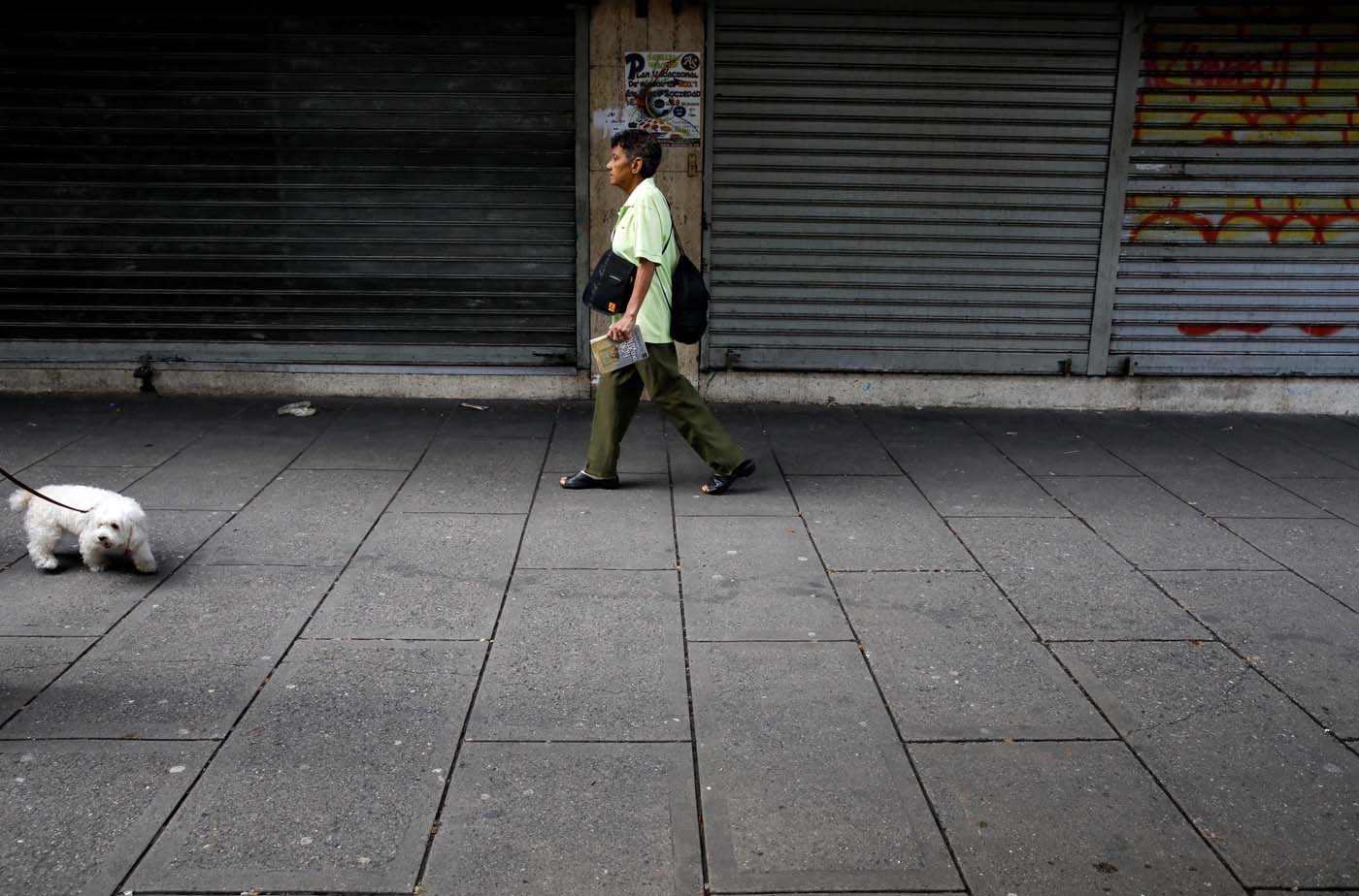 A woman walks on a sidewalk in front of closed business during a strike called to protest against Venezuelan President Nicolas Maduro's government in Caracas, Venezuela, July 20, 2017. REUTERS/Carlos Garcia Rawlins