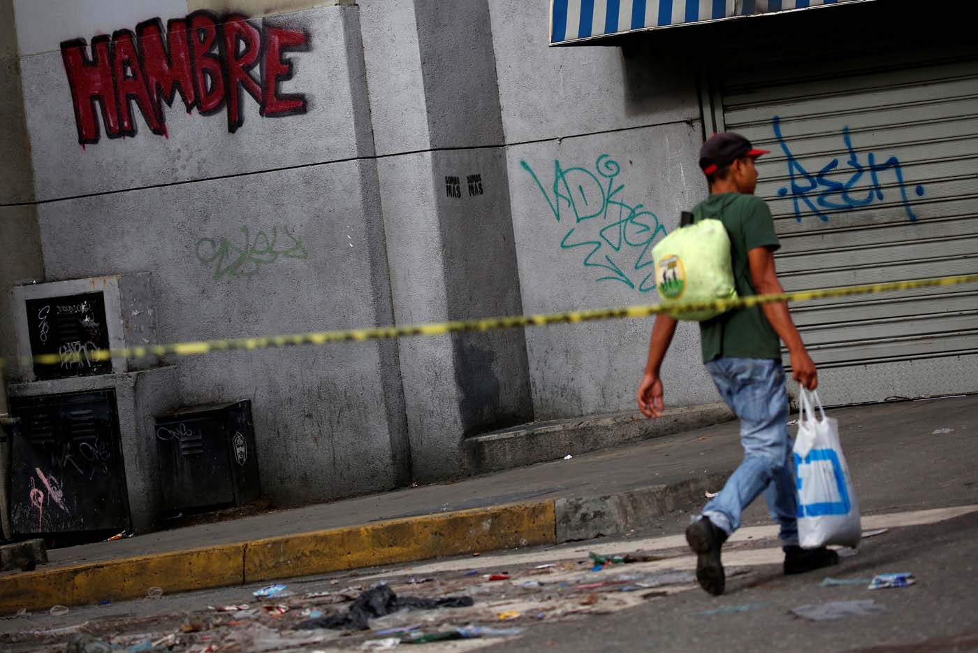A man walks along a closed street near a graffiti that reads "hunger" during a strike called to protest against Venezuelan President Nicolas Maduro's government in Caracas, Venezuela, July 20, 2017. REUTERS/Carlos Garcia Rawlins