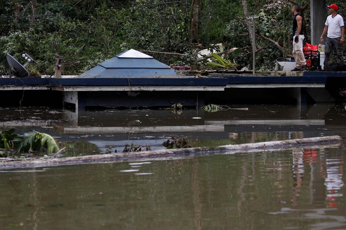 Men stand at the roof of a house submerged by flood waters close to the dam of the Guajataca lake after the area was hit by Hurricane Maria in Guajataca, Puerto Rico September 23, 2017. REUTERS/Carlos Garcia Rawlins