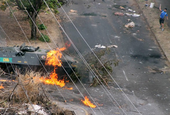 Demonstrator throws rocks at a National Guard tank on fire after being hit by a Molotov cocktail during a protest against President Maduro's government in San Cristobal