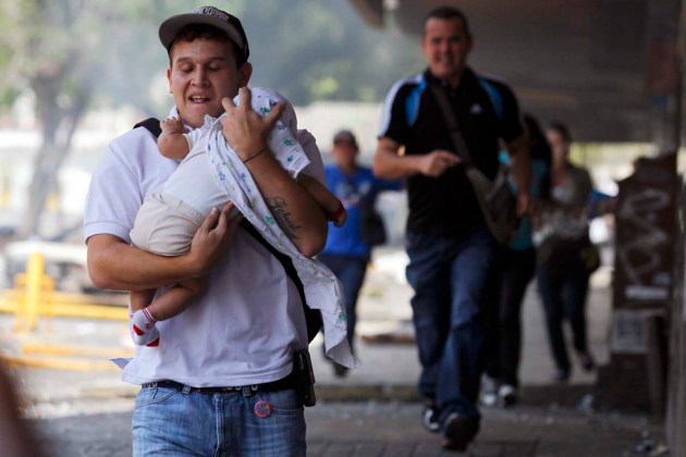 A man runs with a baby to take cover from teargas and stones during riots in Caracas