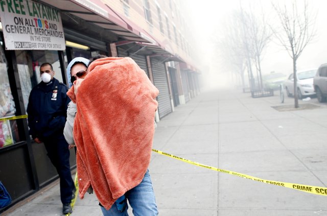 A man carries a child wrapped in a blanket on East 116th street away from an apparent building explosion fire and collapse in the Harlem section of New York City