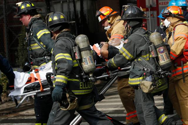 Emergency workers and firefighters use a gurney to transport an injured victim from the site of a building collapse and fire in Harlem