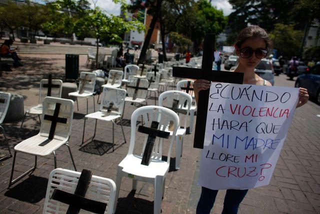 Anti-government protester holds a placard and a black cross, representing victims who died from violence, during a protest in Caracas