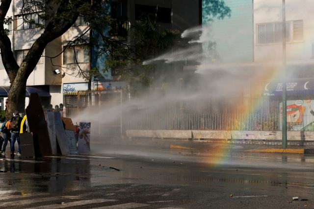 Anti-government protesters are hit by the water cannon during clashes with police at Altamira square in Caracas
