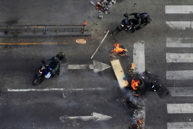 National guards ride their motorbikes past a barricade while looking for anti-government protesters during a protest against Nicolas Maduro's government at Altamira square in Caracas