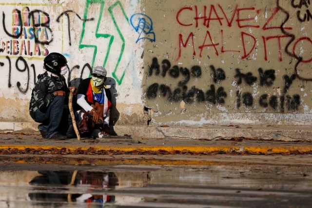 Anti-government protesters take cover next to a wall during clashes with police at Altamira square in Caracas