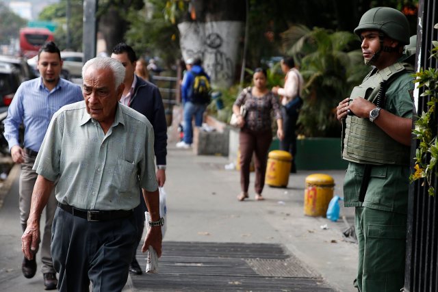 People walk in front of a National Guard at Altamira square in Caracas
