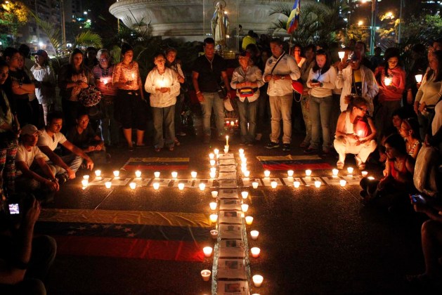 Anti-government protesters place candles next to photographs of victims of violence during a prayer ceremony in Caracas