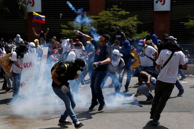 Anti-government protesters throw teargas canisters back at the police in Caracas