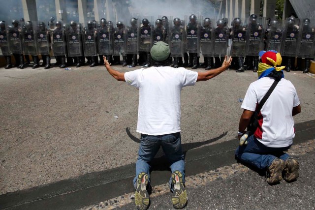 Anti-government protesters kneel and shout in front of riot police during a protest against Maduro's government in Caracas