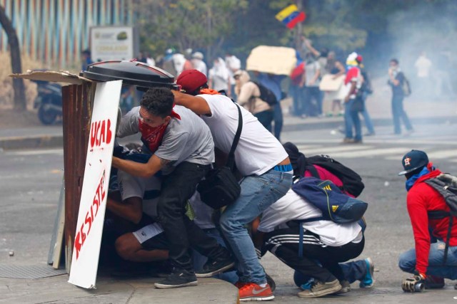 Anti-government protesters take cover behind makeshift shields during clashes with riot police in Caracas