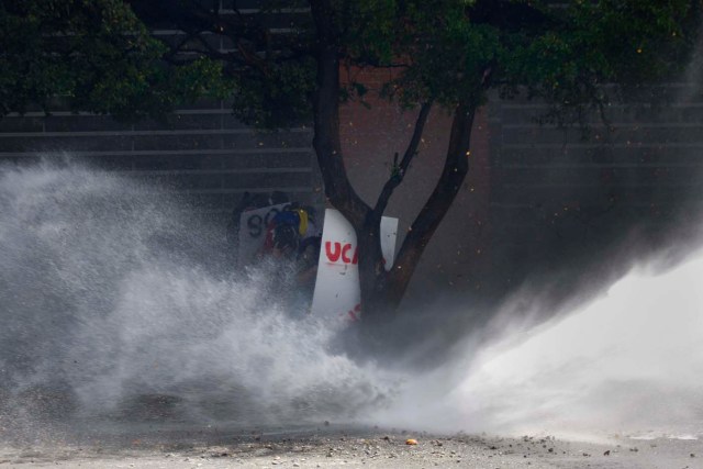 Anti-government protesters take cover from police water cannon in Caracas